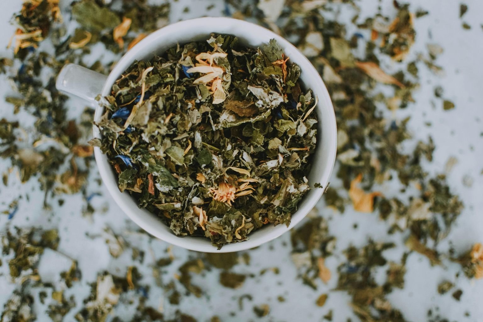 Overhead shot of a cup with a blend of dried herbal tea leaves and flowers. Benefits of Green Tea for Your Wellbeing